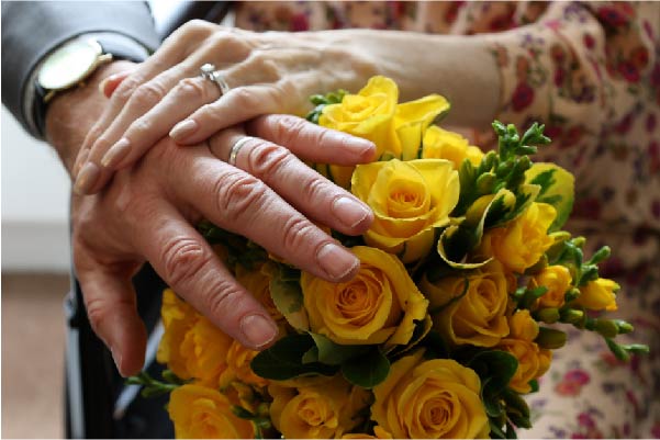 Hospice couple wearing wedding bands and holding bright yellow flowers